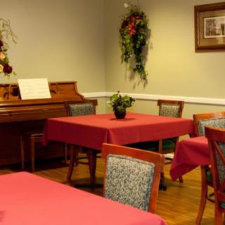 A cozy room with a piano, red tablecloth-covered tables, and decorative wall hangings.