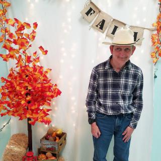 Person in a cowboy hat and plaid shirt enjoying fall decorations.