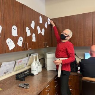 A fun Halloween decoration activity in the office, featuring paper ghosts and a person dressed in costume.