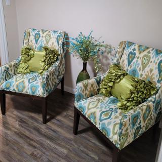 A cozy seating area featuring two patterned armchairs with green accent pillows and a decorative vase.