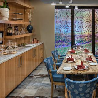 A modern dining room with a beautifully set table, featuring wooden shelves and colorful glass panels.