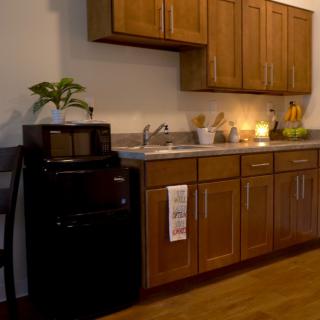 A cozy kitchen with wooden cabinets, a sink, microwave, and a small refrigerator.