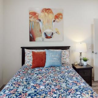 A cozy bedroom featuring a colorful cow painting above the bed with floral bedding and decorative pillows.