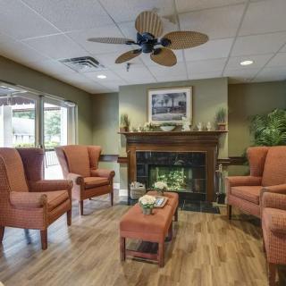 A cozy living room with armchairs arranged around a fireplace and a ceiling fan overhead.