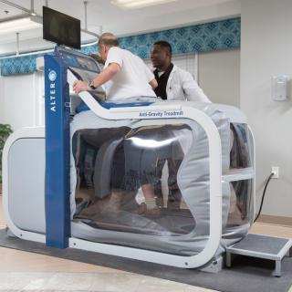 A person using an anti-gravity treadmill under the supervision of a trainer in a rehabilitation setting.