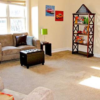 A cozy living room with a sofa, coffee table, bookshelf, and bright natural light from large windows.