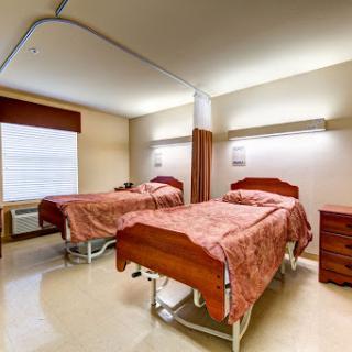 A spacious and well-lit hospital patient room featuring two beds with bedside tables.
