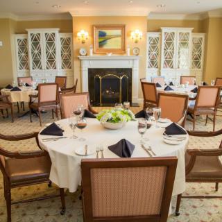 An elegantly set dining room with round tables, upholstered chairs, and a fireplace.