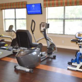 A well-equipped gym with exercise machines, including a treadmill and stationary bikes, in a bright indoor setting.