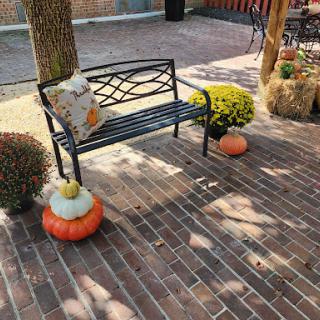 A cozy outdoor setting with a decorative bench surrounded by autumn-themed elements like pumpkins and flowers.