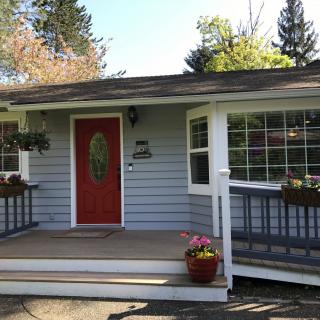 A charming single-story house with a red front door, surrounded by windows and decorated with plants on the porch.