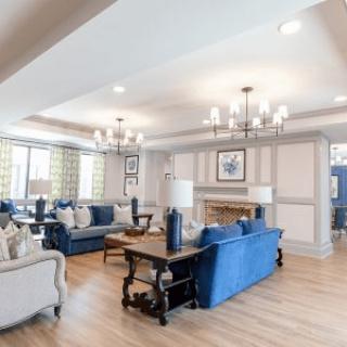 A spacious and elegantly decorated living room with blue sofas, chandeliers, and wood flooring.