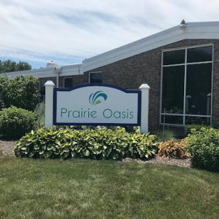 Prairie Oasis sign in front of a modern building surrounded by lush greenery.