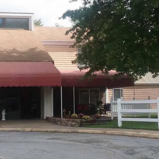 A building entrance with a red awning and driveway surrounded by greenery.