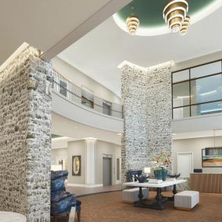 A modern lobby interior featuring a high ceiling and stone wall with stylish furniture and lighting.
