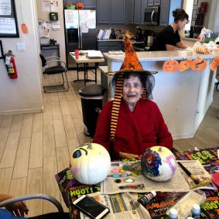 A joyful celebration of Halloween with a senior lady in a witch hat surrounded by decorated pumpkins.