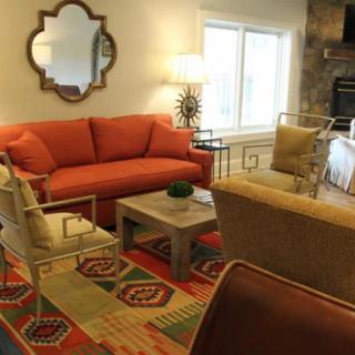 A cozy living room featuring a red sofa, decorative mirror, patterned rug, and various seating options.