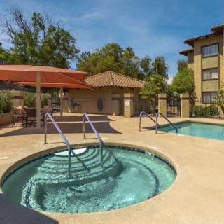 A relaxing outdoor area featuring a hot tub and pool at an apartment complex on a sunny day.