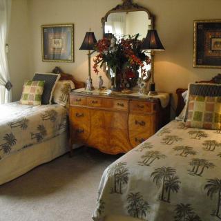 A cozy bedroom with twin beds and a vintage dresser adorned with lamps and flowers.
