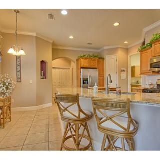 A modern kitchen interior featuring bar stools at a large countertop, with stylish lighting and stainless steel appliances.