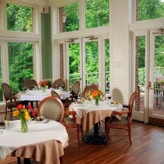 Elegant restaurant interior with tables and chairs, adorned with flowers and natural light streaming through large windows.
