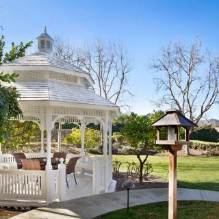 A picturesque white gazebo in a sunny garden with a birdhouse nearby.