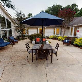 A cozy outdoor patio area with a table, chairs, and an umbrella surrounded by well-maintained landscaping.