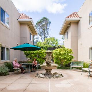 A serene courtyard with a fountain and outdoor seating, surrounded by two buildings.
