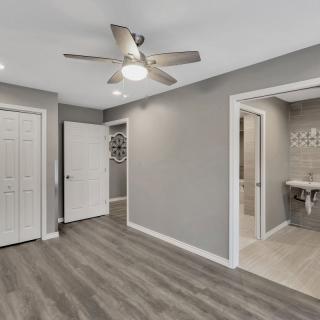 A modern bedroom featuring laminate flooring, a ceiling fan, and neutral color palette. The room includes a closet and an en-suite bathroom.
