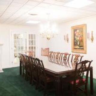 A well-lit dining room with a large table, surrounded by chairs and adorned with a chandelier and artwork.