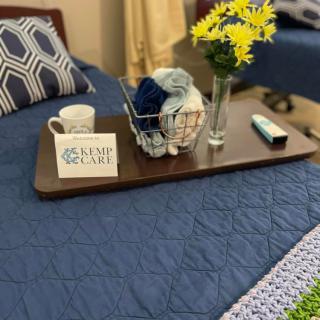 A cozy setup with a tray on a bed featuring a coffee mug, yarn basket, and a vase of yellow flowers.