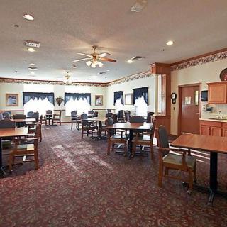 A spacious dining room with neatly arranged tables and chairs, featuring carpeted flooring and large windows with curtains.