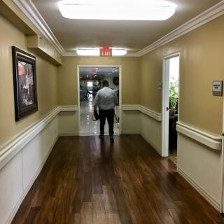 A person walks down a well-lit hallway with wooden floors and framed artwork on the walls.