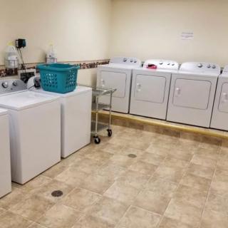 A laundry room with washing machines, dryers, and a laundry basket on a tiled floor.
