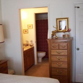 Cozy bedroom with a view into an adjacent bathroom, featuring wooden furniture and soft lighting.
