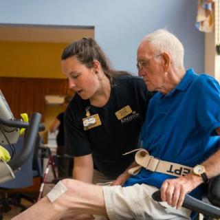 A healthcare professional assists an elderly person during a physical therapy session.