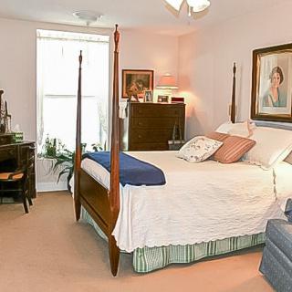 A cozy bedroom with a four-poster bed, decorated with paintings and traditional furniture.