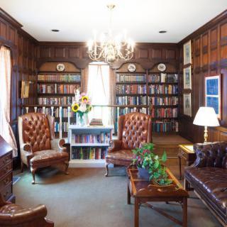 A cozy and elegant library room with leather chairs, a chandelier, and walls lined with bookshelves.