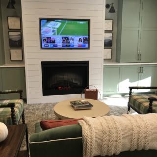 A cozy living room with a TV mounted above a fireplace, surrounded by comfortable seating and a central coffee table.