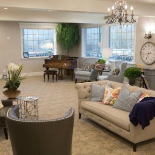 A well-decorated living room featuring a sofa, piano, and chandelier with large windows.