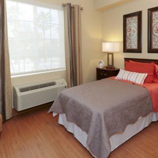 A cozy bedroom with a neatly made bed, two decorative pictures on the wall, and natural light coming through the window.