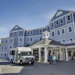 A large, multi-story building with a shuttle bus parked in front and people entering.