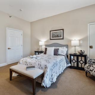 A cozy bedroom featuring a neatly made bed with decorative pillows, nightstands with lamps on both sides, and a comfortable chair in the corner.