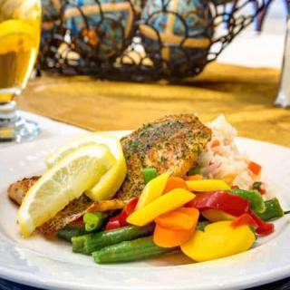 A plate of grilled fish topped with a lemon slice, served with colorful vegetables.