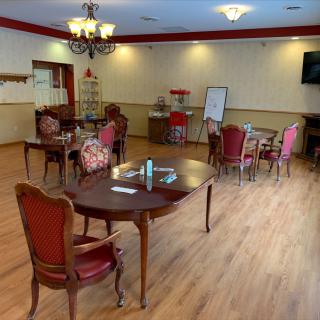 A dining room with elegant chairs, tables, and a chandelier, featuring a wooden floor and a whiteboard.