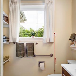 A small bathroom with a window, towels, toilet paper, and a handrail by the toilet.