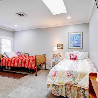 A cozy bedroom with two beds featuring colorful quilts and decorative pillows, illuminated by a table lamp beneath a framed artwork.