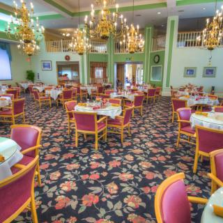 An elegant dining area with floral carpet and chandeliers, featuring neatly arranged tables and chairs.