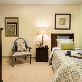 A cozy bedroom with a neatly made bed, upholstered chair, and ambient lighting.
