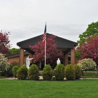 A building with an American flag, surrounded by statues, shrubs, and blossoming trees.